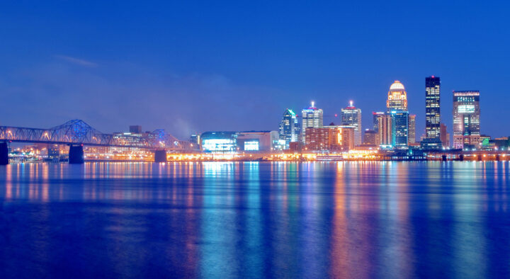 Night view of Louisville, Kentucky skyline reflecting over water, highlighting the area’s urban landscape potentially near the Kentucky Derby location.