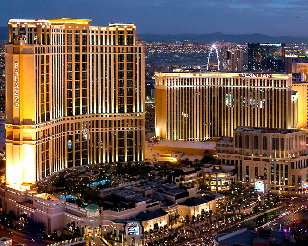 Nighttime view of illuminated Las Vegas hotels, prominently featuring The Palazzo and The Venetian, bustling with activity.