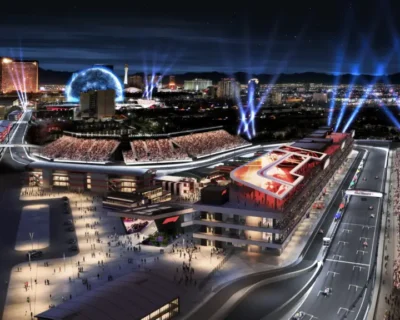 Nighttime rendering of a vibrant Las Vegas street scene featuring massive crowds, illuminated hotels, and a prominent event setup with light beams highlighting the Grand Prix circuit layout.