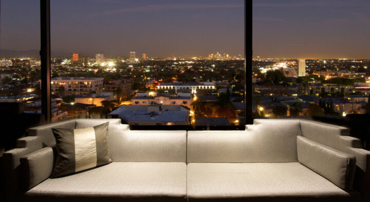 A luxurious hotel guestroom in Los Angeles, featuring a modern, plush sofa in front of floor-to-ceiling windows that offer a stunning night view of the cityscape, ideal for World Cup travelers.