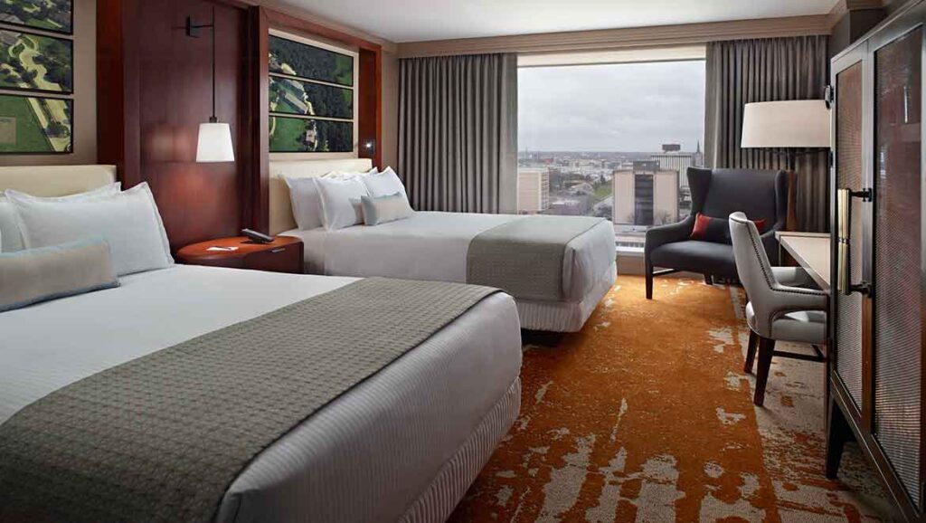 Luxury hotel room with two double beds, a sitting area, and a city view at Omni Louisville, located near Churchill Downs, ideal for Kentucky Derby accommodations.