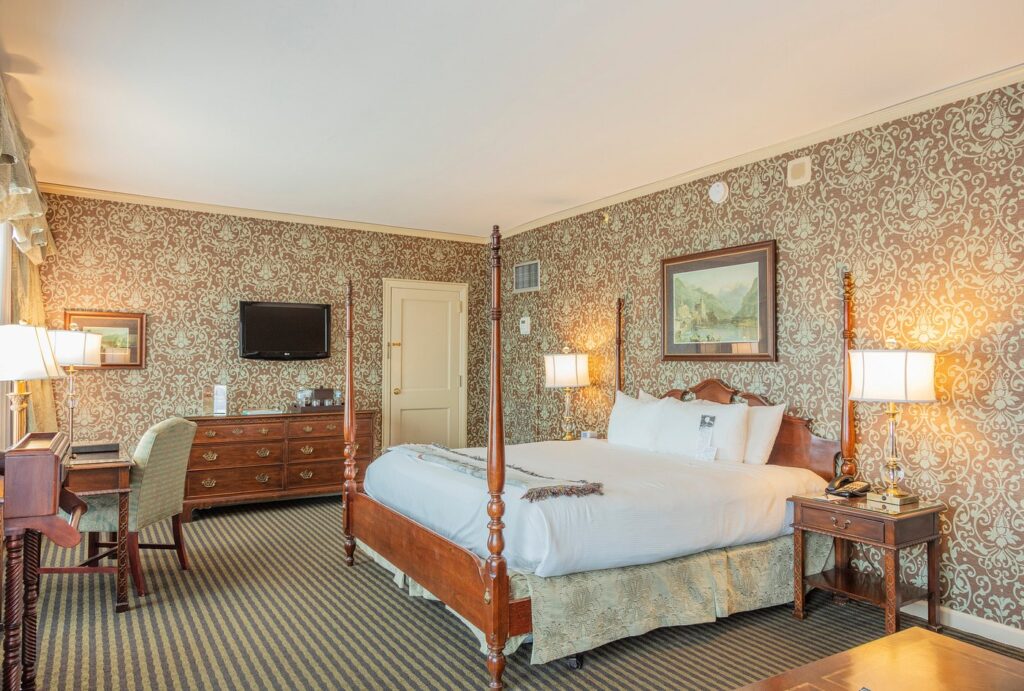 Luxury king-sized bedroom in The Brown Hotel, Louisville, depicting a classic four-poster bed, patterned wallpaper, and elegant furnishings, ideal for visitors to the Kentucky Derby near Churchill Downs.