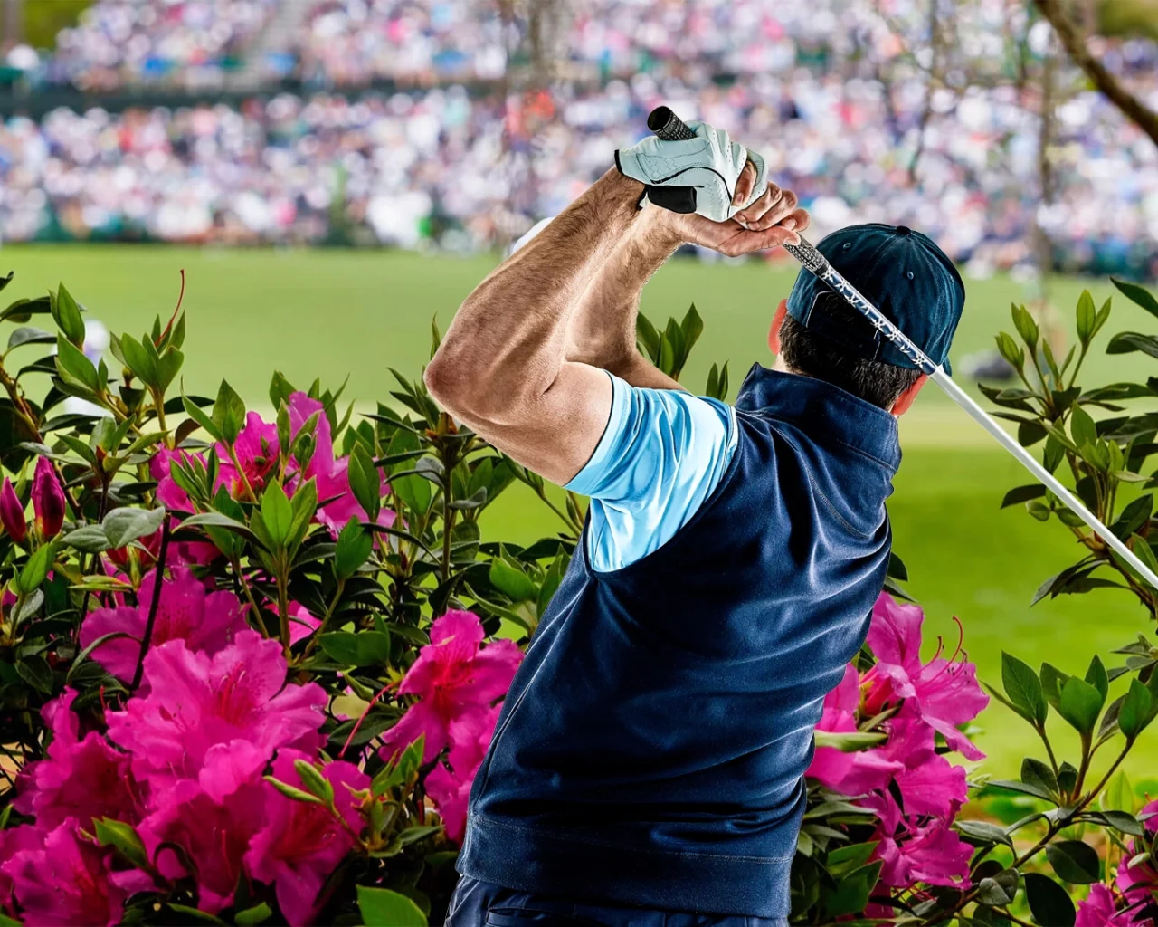 A golfer at Augusta National Golf Club adjusts his cap, surrounded by vibrant flowers, with a blurred crowd of spectators in the background.
