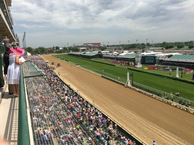 Spectators watch a horse race from the stands at Churchill Downs, highlighting the vibrant atmosphere and expansive setting of the Kentucky Derby, known for its premium tickets, travel, and hotel packages.