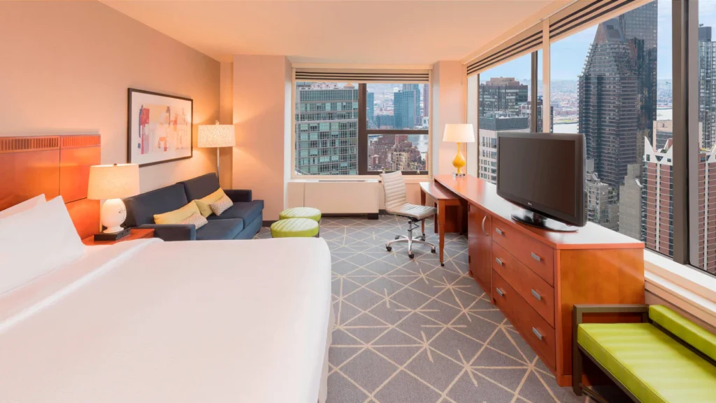 Bright hotel room at Courtyard Midtown East, New York, featuring modern decor with a scenic city view through the window, ideal for visitors of the US Open Tennis event.