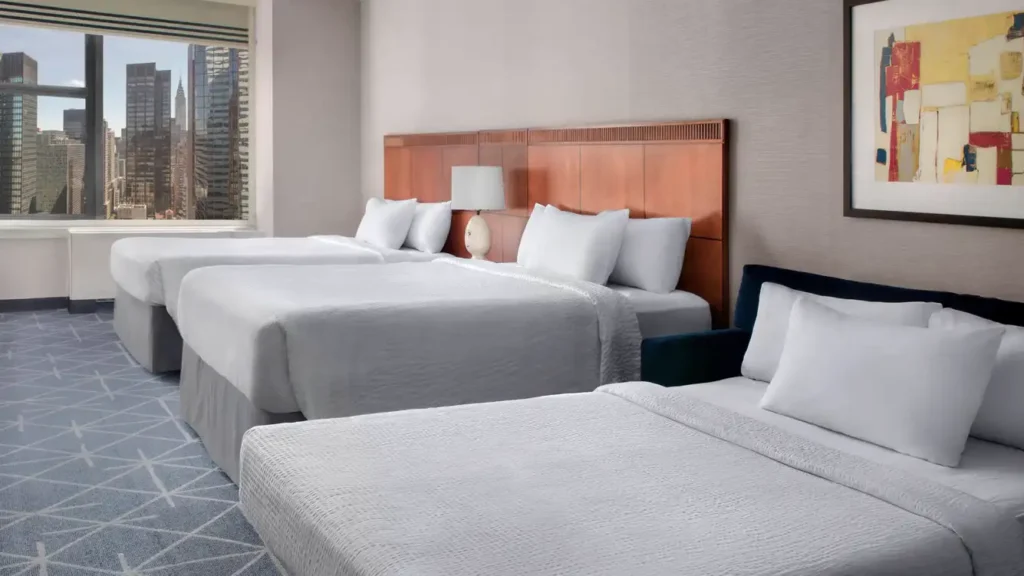 This luxurious hotel room features two queen-sized beds, stylish decor, and large windows offering a stunning view of the New York city skyline, ideal for guests attending the US Open Tennis event.