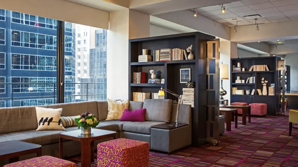 View of a stylish lobby area at the Courtyard Midtown East on Third Avenue, New York, featuring comfortable seating, bookshelves, and large windows with city views, near US Open Tennis accommodations.