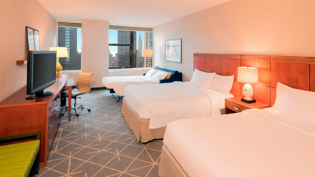 Spacious, modern hotel room with two double beds, large windows showcasing New York City skyline views, ideal for visitors to nearby US Open Tennis at Courtyard Midtown East.