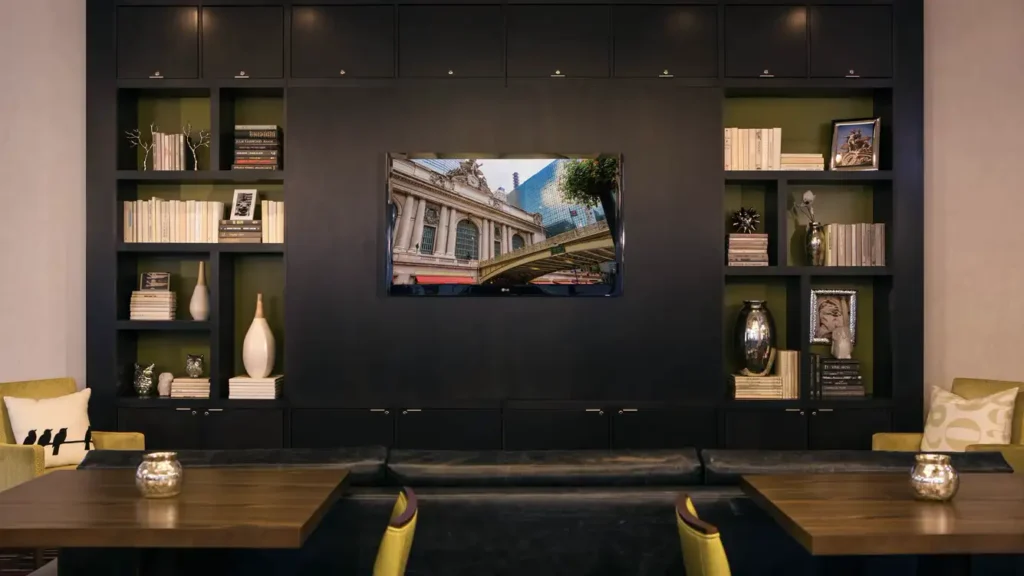 Luxury hotel lobby in New York features a stylish seating area with a large black bookshelf, decorative items, and a wall-mounted photograph of a grand building.
