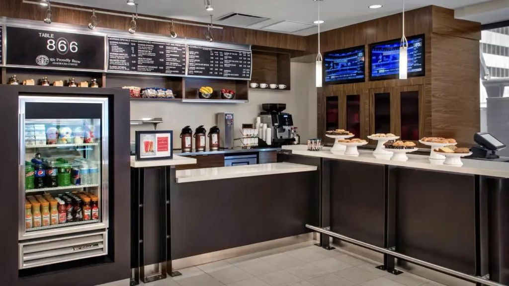 Inside the Courtyard Midtown East at 866 Third Avenue, New York, a modern café displays beverages, snacks, and freshly baked pies under a menu sign that includes Starbucks coffee.