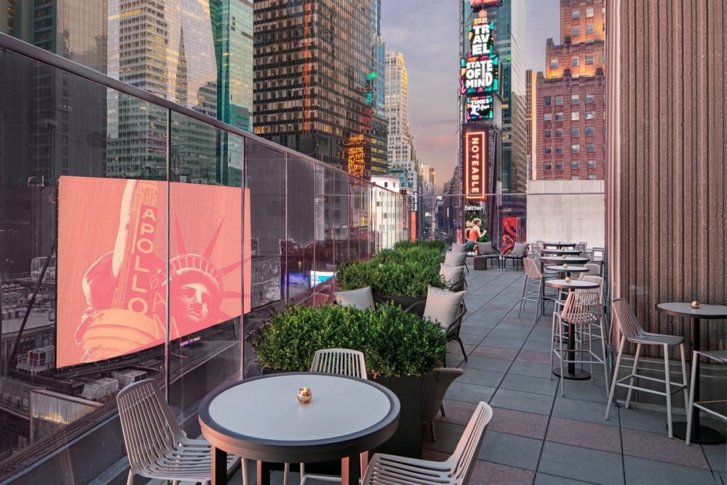 Outdoor lounge area at the New York Marriott Marquis overlooking Broadway, featuring modern furniture, glass barriers, and vibrant city views, perfect for visitors attending the US Open Tennis event.