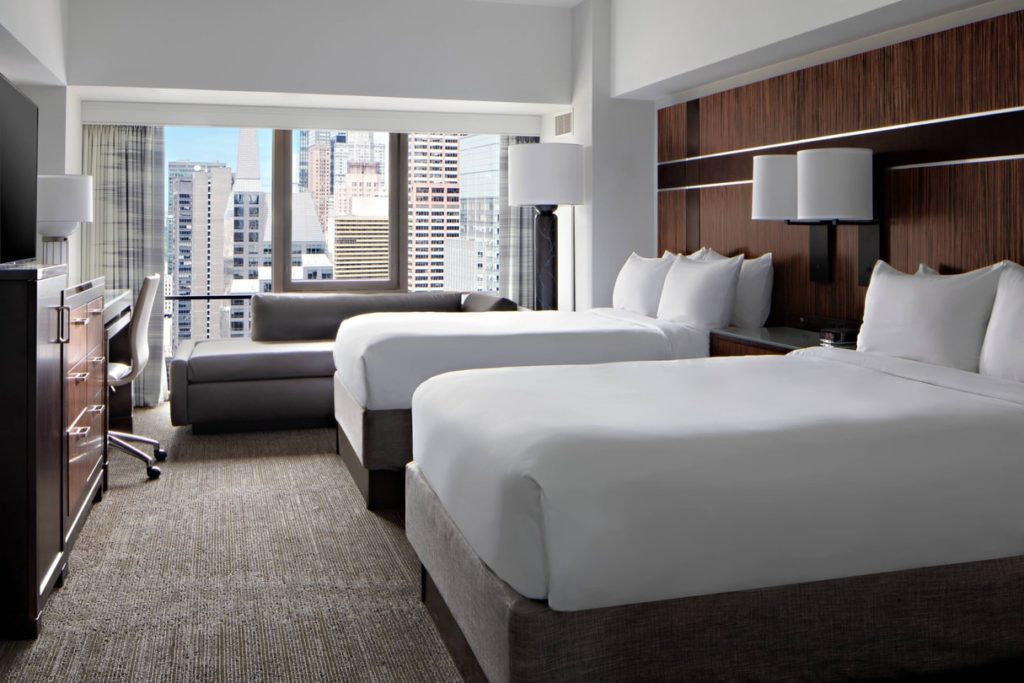 Luxury hotel room at the New York Marriott Marquis showing two queen beds, modern furniture, and a view of the city's skyline, ideal for visitors attending the US Open Tennis.