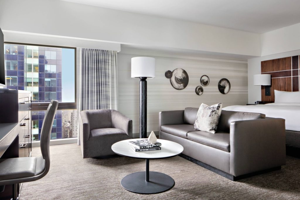 Luxurious guestroom at the New York Marriott Marquis featuring modern furniture, artistic wall decor, and a view of the cityscape, ideal for US Open Tennis accommodations in New York.