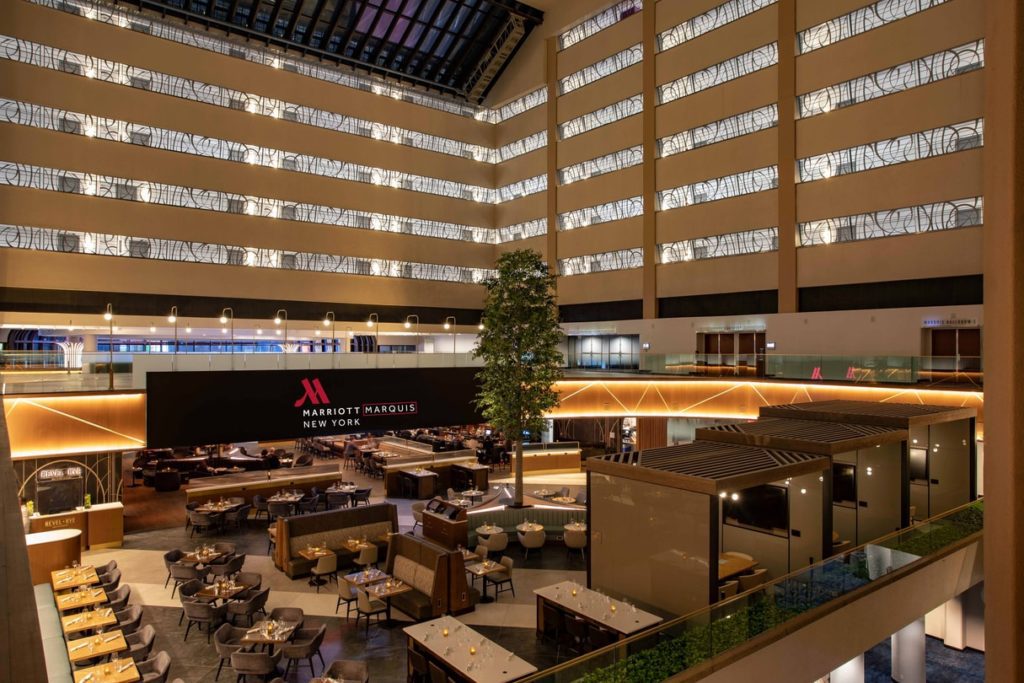 Interior view of the New York Marriott Marquis showing a spacious atrium with multiple levels, a large seating area, and illuminated signage.
