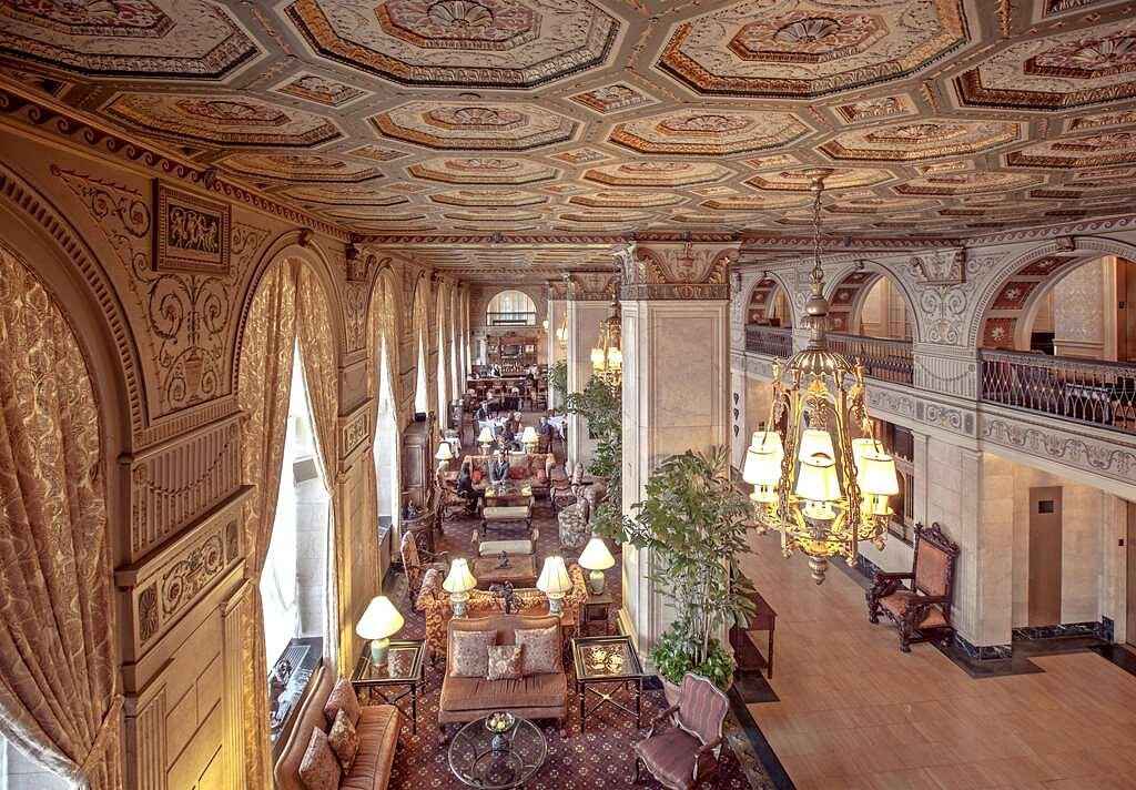 Luxurious hotel lobby at The Brown Hotel in Louisville, showcasing an ornately decorated ceiling, elegant chandeliers, and guests relaxing in a sophisticated setting, ideal for Kentucky Derby accommodations.