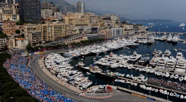 Crowds line the street circuit at the Monaco Grand Prix surrounded by luxury yachts and high-rise buildings, highlighting the prestigious event's vibrant atmosphere.