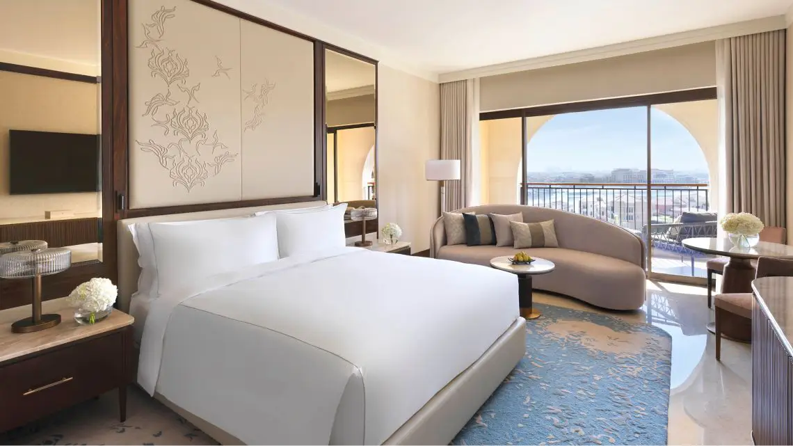 Luxurious hotel room at Ritz-Carlton Abu Dhabi, featuring a plush king-sized bed, stylish seating area, and a scenic balcony view, ideal for guests visiting the Abu Dhabi Grand Prix.