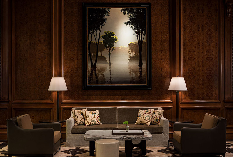 Inside the Ritz-Carlton Central Park, an elegant lounge area features comfortable seating and a striking framed painting of a serene, misty lakescape illuminated by soft lighting. Ideal for guests visiting New York for the US Open Tennis.