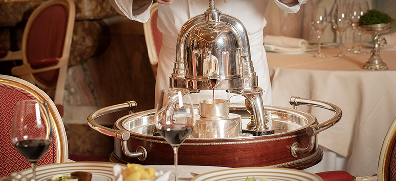 Waiter serving from a fancy trolley in a luxury dining setting at The Ritz London, a popular choice for accommodations during the Wimbledon Championships in London, England.