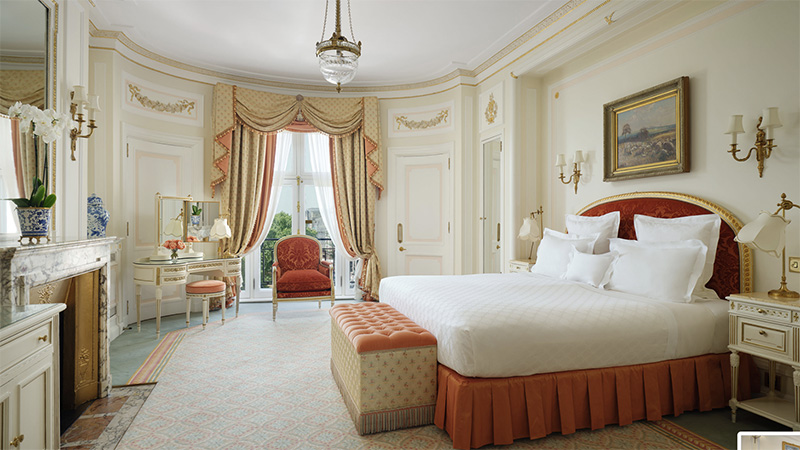 Luxurious guest room at The Ritz London featuring a large bed with red headboard, ornate decor, and elegant furniture, ideal for visitors attending the Wimbledon Championships.