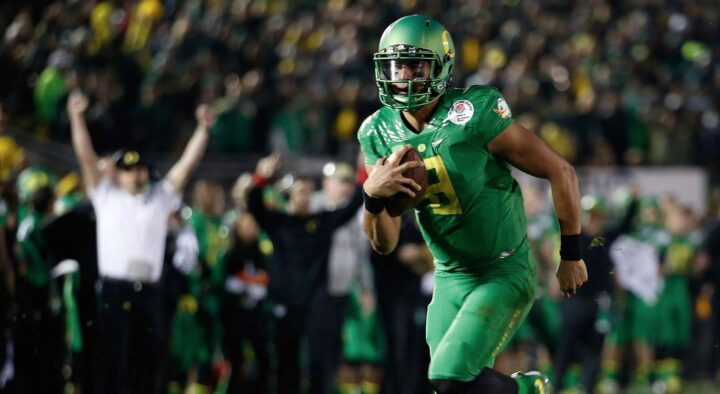 A football player in a green uniform runs with the ball during a game at the Rose Bowl in Pasadena, CA, surrounded by cheering fans.