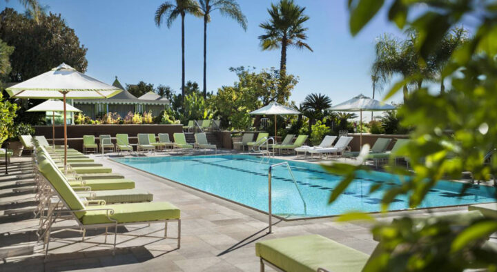 Luxury hotel in Pasadena featuring a large outdoor swimming pool lined with green lounge chairs and umbrellas, ideal for visitors attending events at the nearby Rose Bowl.