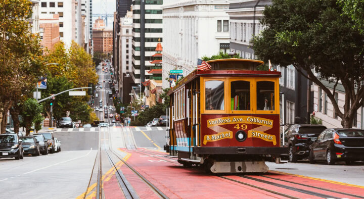 A cable car travels along Van Ness Avenue in San Francisco, surrounded by cars and buildings, illustrating a typical urban scene in a major city.