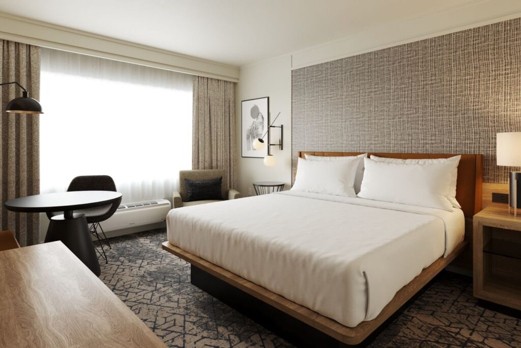 Elegantly furnished hotel room featuring a large bed, textured wallpaper, and modern furniture, located at the Sheraton Augusta Hotel on Stevens Creek Road, a convenient accommodation choice for visiting Augusta, GA.