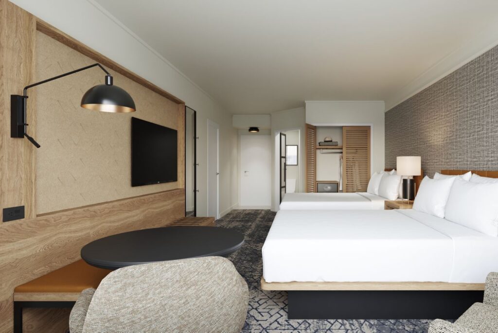 Modern hotel room featuring two beds with pristine white bedding, a rustic wooden accent wall with a mounted TV, and a cozy seating area, ideal for accommodations in Augusta near Masters golf events.