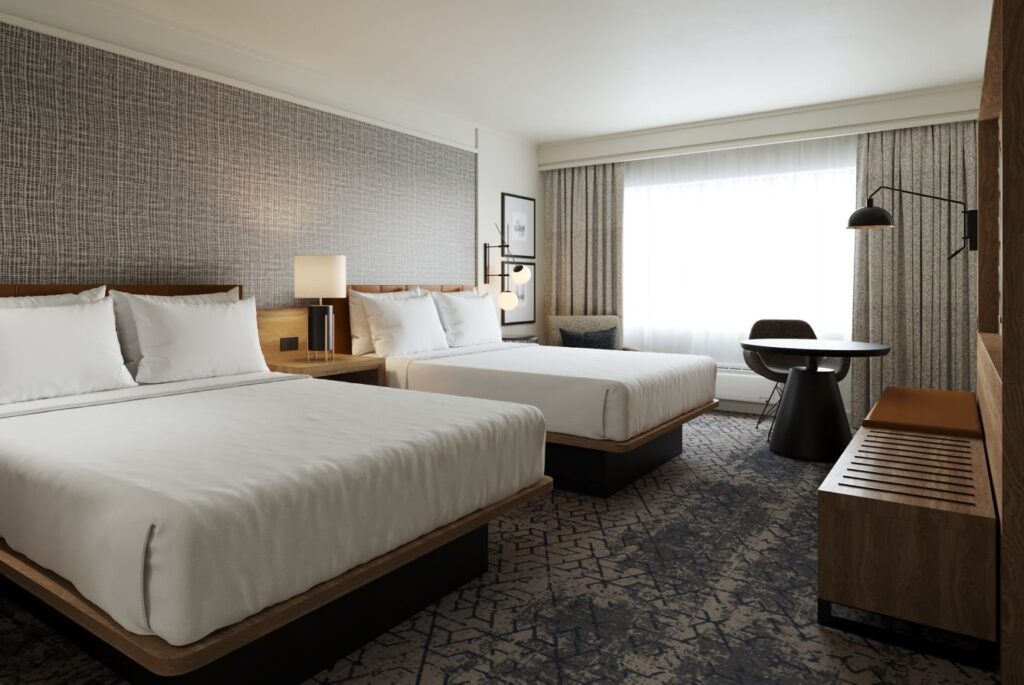 Elegant guest room featuring two queen beds with white bedding, stylish furnishings, and a large window, located at Sheraton Augusta Hotel, a choice accommodation for Augusta hotels and Greensboro visitors.