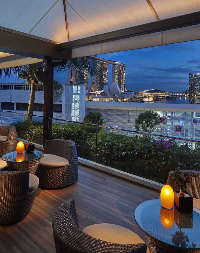 An elegant outdoor terrace at a luxury hotel in Singapore, overlooking the iconic Marina Bay Sands, offers a scenic dining experience for guests attending the Singapore Grand Prix.