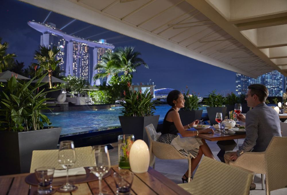 A couple enjoys a fine dining experience at Dolce Vita terrace in Singapore, with a view of the Marina Bay Sands, ideal accommodation for guests attending the Singapore Grand Prix.