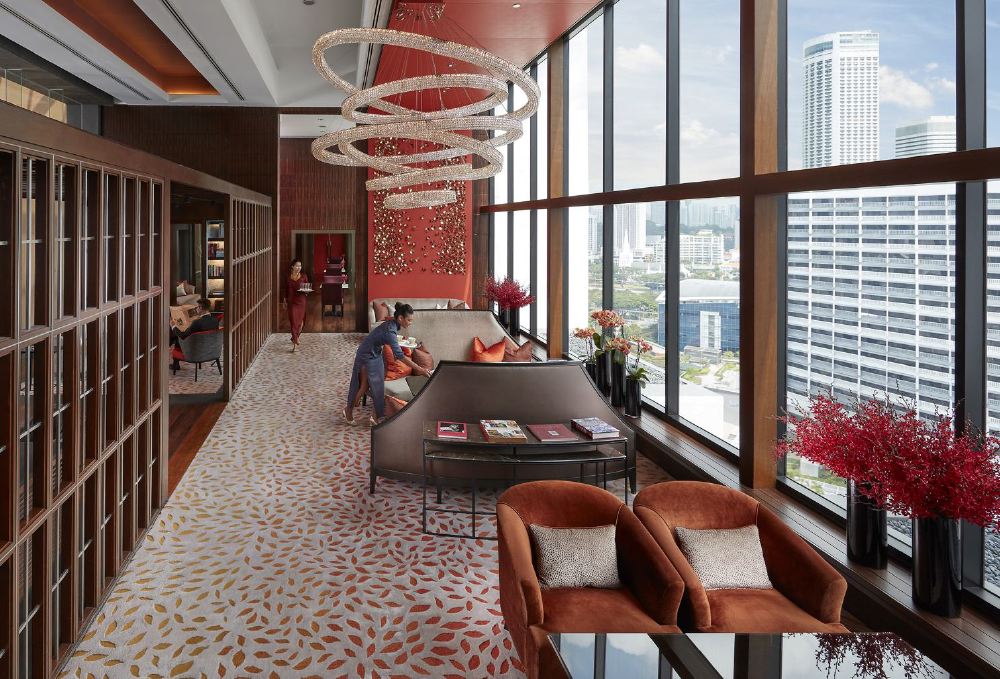 Elegant hotel lounge in Singapore with guests relaxing, featuring modern decor, large windows overlooking the city, and distinctive circular chandeliers, ideal for those seeking luxury accommodations near the Singapore Grand Prix.