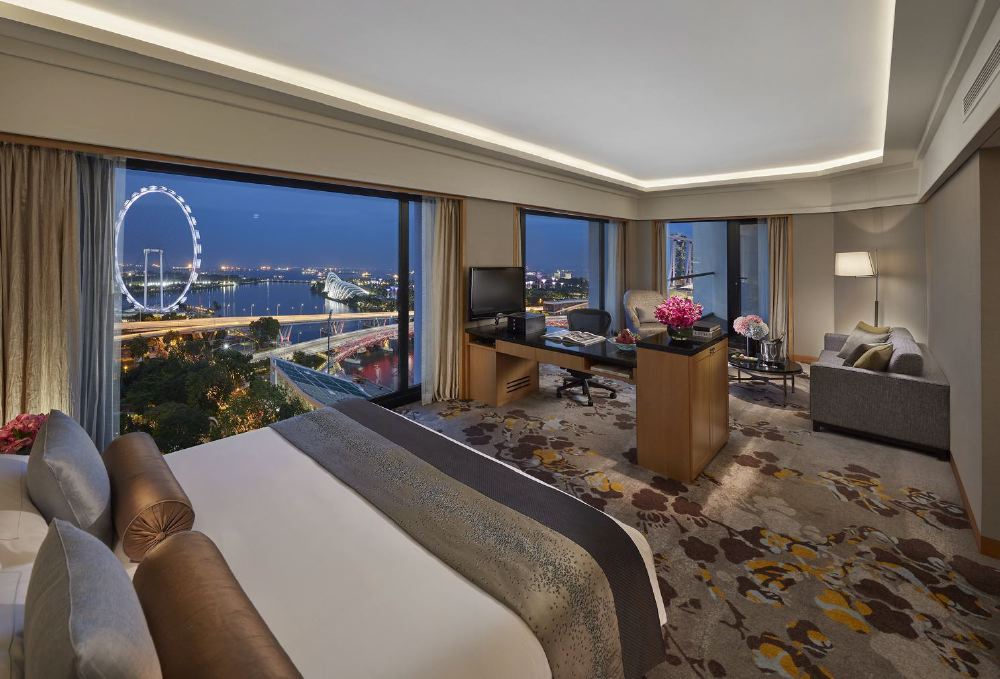 A luxurious hotel room in Singapore with a large window showcasing a nighttime view of the Singapore Flyer and cityscape, ideal for visitors attending the Singapore Grand Prix.