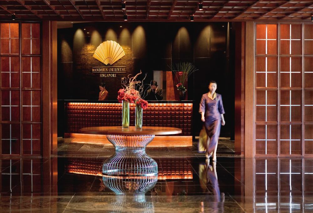 Luxury lobby of the Mandarin Oriental in Singapore, displaying rich wooden décor and an elegant staff member walking, ideal for visitors attending the Singapore Grand Prix.