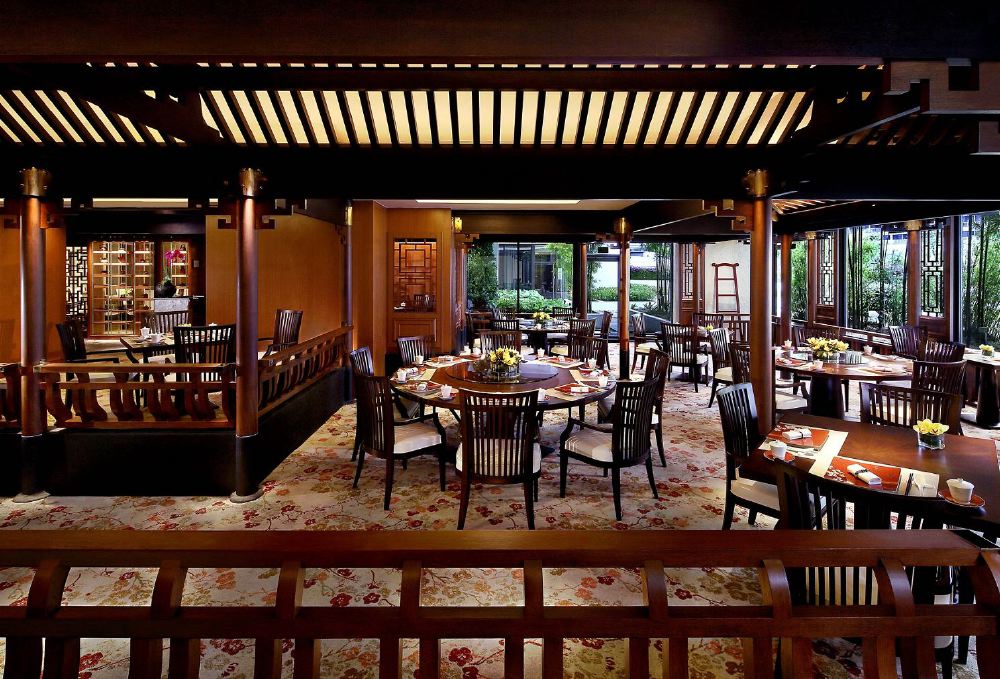 Elegant dining room at Mandarin Oriental, Singapore, featuring traditional décor, a wooden ceiling, and large windows with garden views, ideal for visitors seeking luxury accommodations near the Singapore Grand Prix.