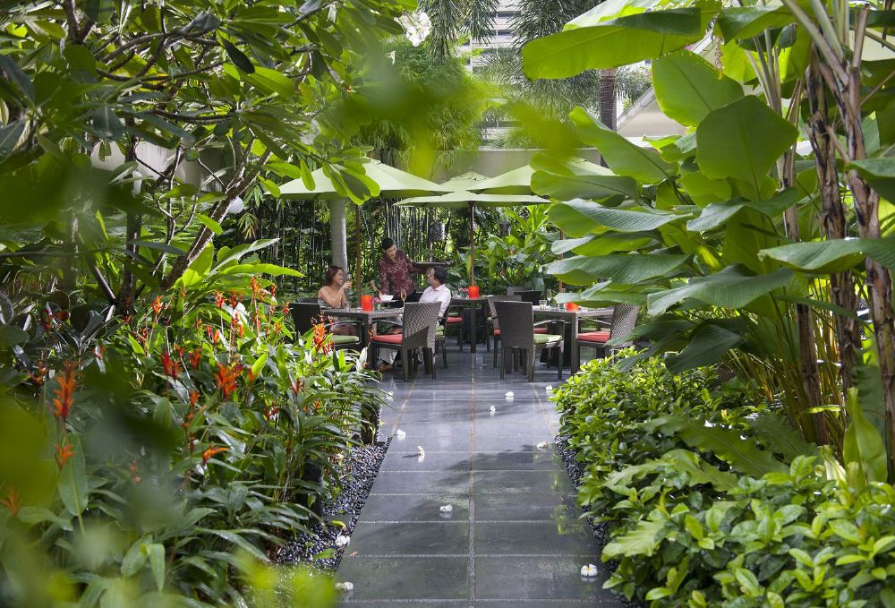 Guests dine outdoors at Melt the World Cafe, nestled among lush greenery at the Mandarin Oriental on Raffles Avenue, a popular spot for luxury accommodations in Singapore.