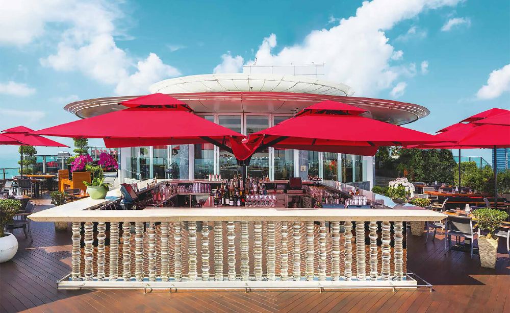 Luxury rooftop bar with red umbrellas and a panoramic sea view at Marina Bay Sands, a key accommodation spot for Singapore Grand Prix enthusiasts.