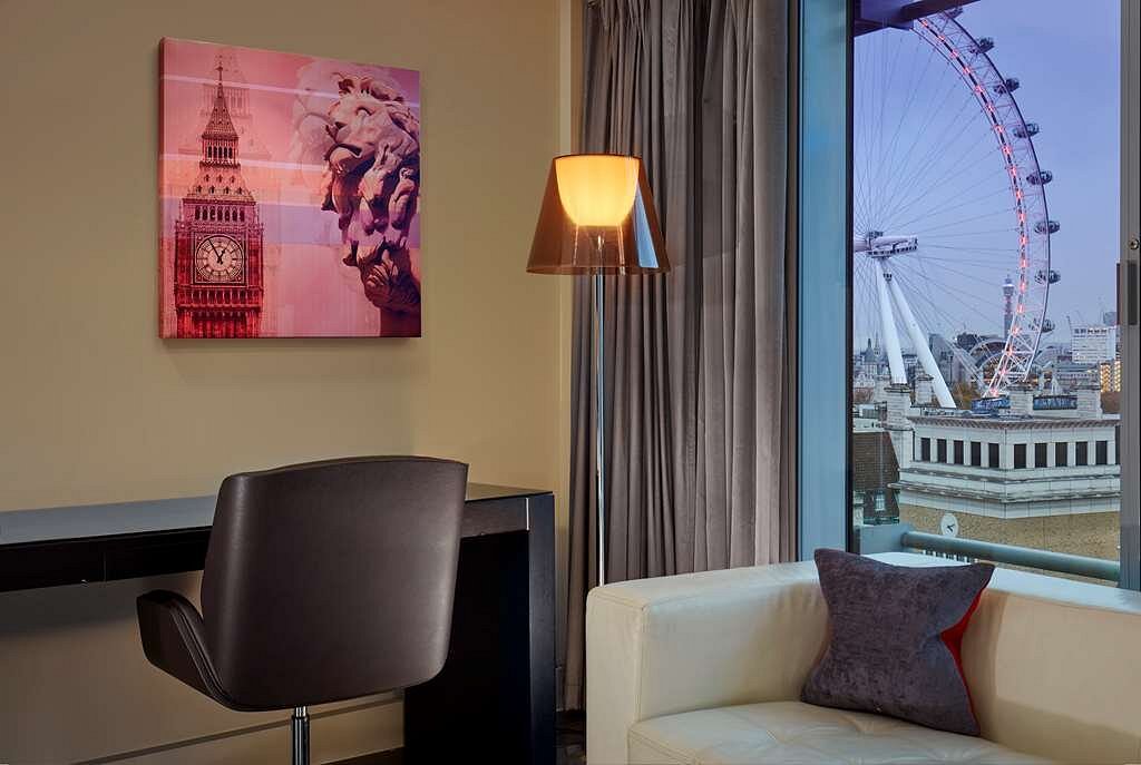 View of the London Eye from a luxury hotel room featuring a chair, desk, and a colorful artwork of Big Ben on the wall, situated near Park Plaza Westminster Bridge.