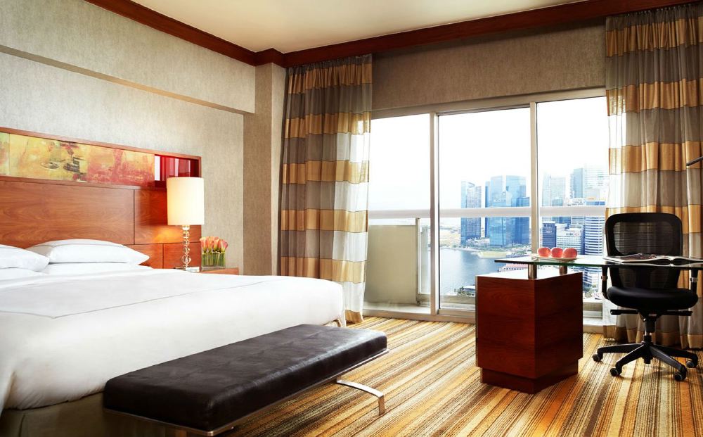 View of a luxurious hotel room at Swissotel The Stamford in Singapore, featuring modern decor and a large window overlooking the Marina Bay area, ideal accommodation for the Singapore Grand Prix.