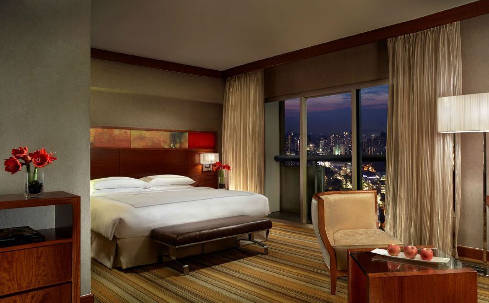 Luxurious hotel room at Swissotel The Stamford in Singapore, featuring a king-sized bed, contemporary furnishings, and a stunning night view of the city skyline, ideal for visitors to the Singapore Grand Prix.