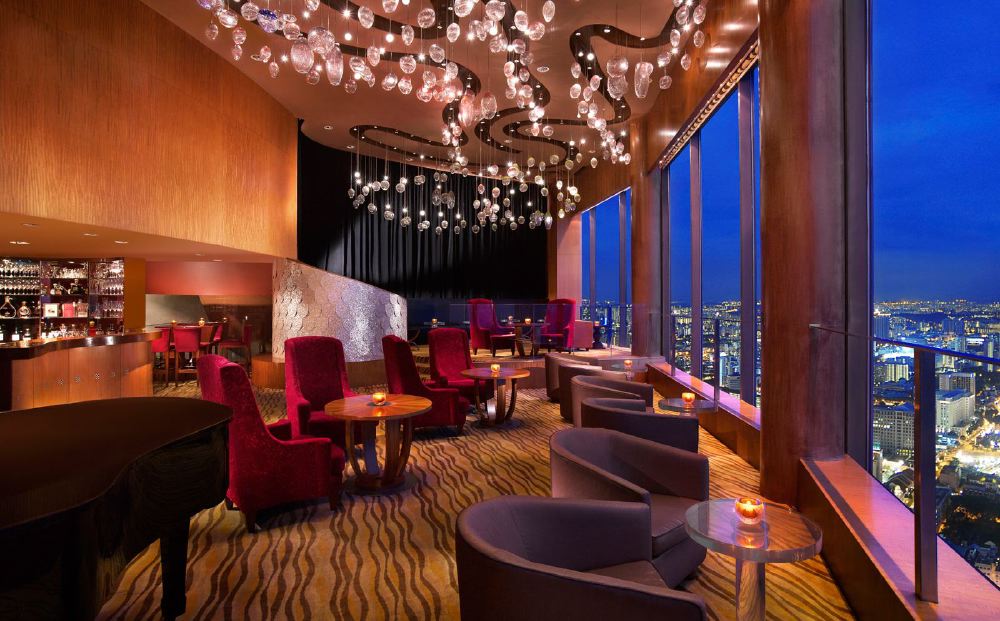 Interior of a luxurious bar at Swissotel The Stamford in Singapore, featuring elegant chandeliers, comfortable seating, and a striking night view of the city, ideal for visitors looking for accommodations near the Singapore Grand Prix.