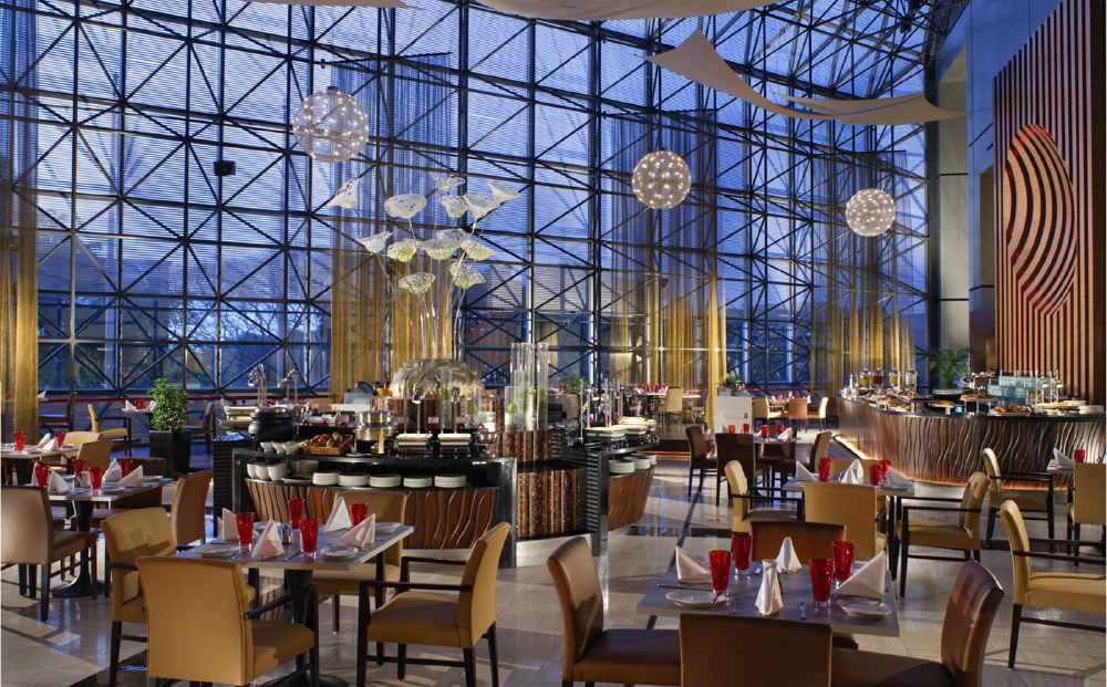 Interior view of a dining area in Swissôtel The Stamford, featuring neatly arranged tables and chairs, expansive glass walls, and modern lighting, ideal for guests visiting during the Singapore Grand Prix.
