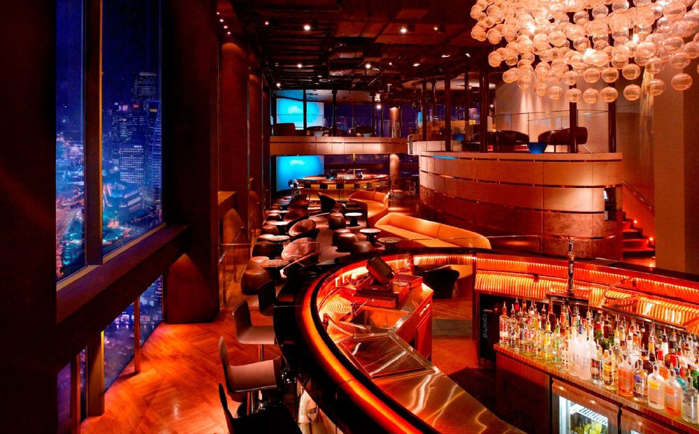 Inside Swissotel The Stamford in Singapore, a luxurious bar area overlooks the city skyline, featuring a well-stocked bar counter, cozy seating arrangements, and modern decor, ideal for Singapore Grand Prix visitors.