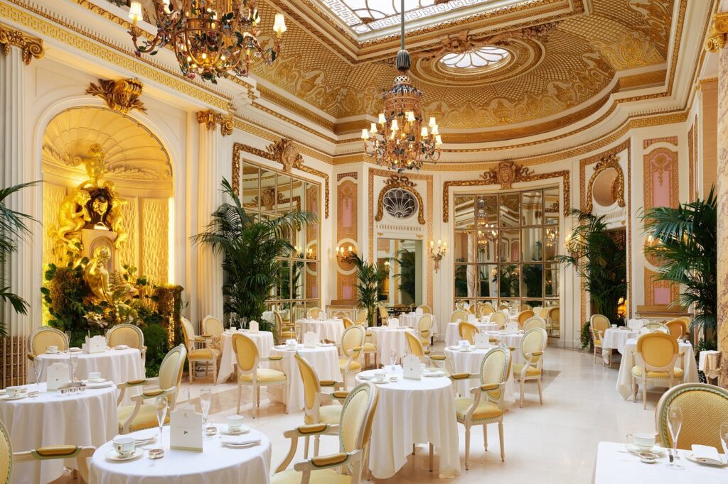 Elegant dining area in The Ritz London, featuring opulent decor with golden statues, intricate ceilings, and an arrangement of white-clothed tables, ideal for guests visiting during the Wimbledon Championships.