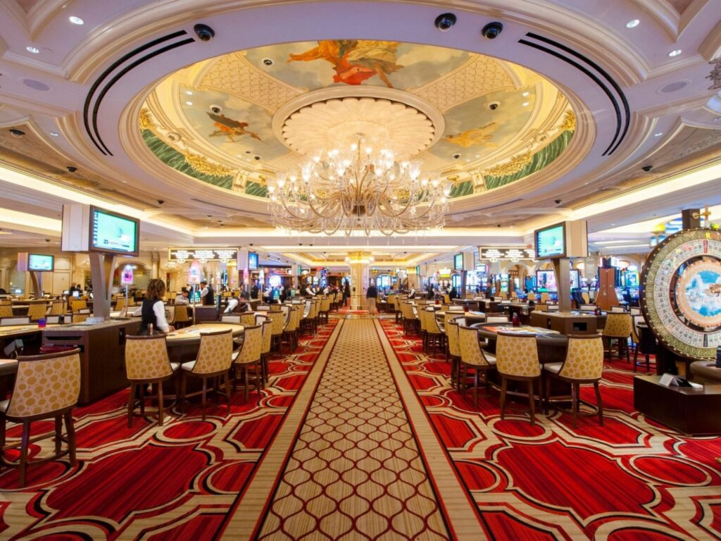 Luxurious interior of The Venetian Resort in Las Vegas, showcasing a spacious casino floor with elegant decor, gaming tables, and a large chandelier.