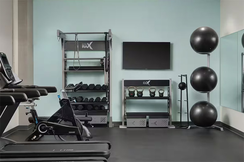 Modern gym at Tru by Hilton Indianapolis Downtown, featuring treadmills, weights, and exercise balls.