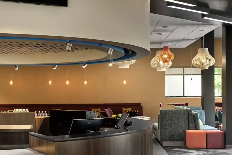 A spacious, stylish lobby at Tru by Hilton Indianapolis Downtown, featuring a curved desk, modern hanging lights, and vibrant seating, ideal for visitors of the Indianapolis 500.