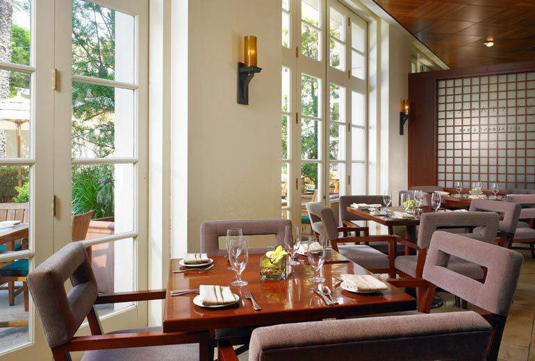 Elegant dining area with set tables, large vertical windows, and modern decor in a luxury hotel in Pasadena, convenient for Rose Bowl visitors.