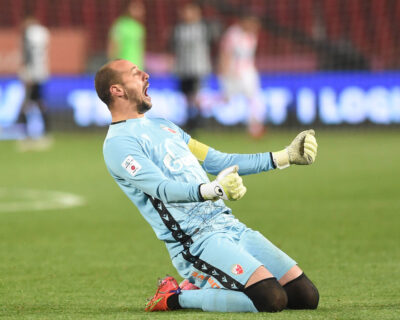 A goalkeeper in a light blue uniform celebrates during a soccer match, likely a crucial save or victory, exemplifying the intensity and excitement of World Cup soccer games.